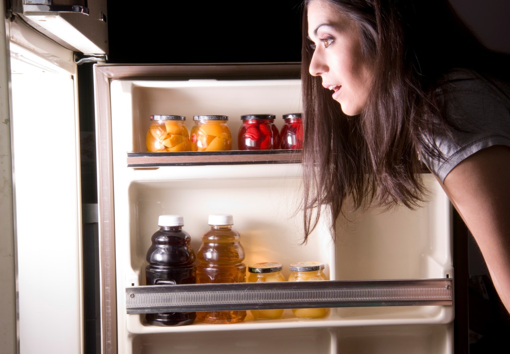 Mulher olhando a geladeira à noite