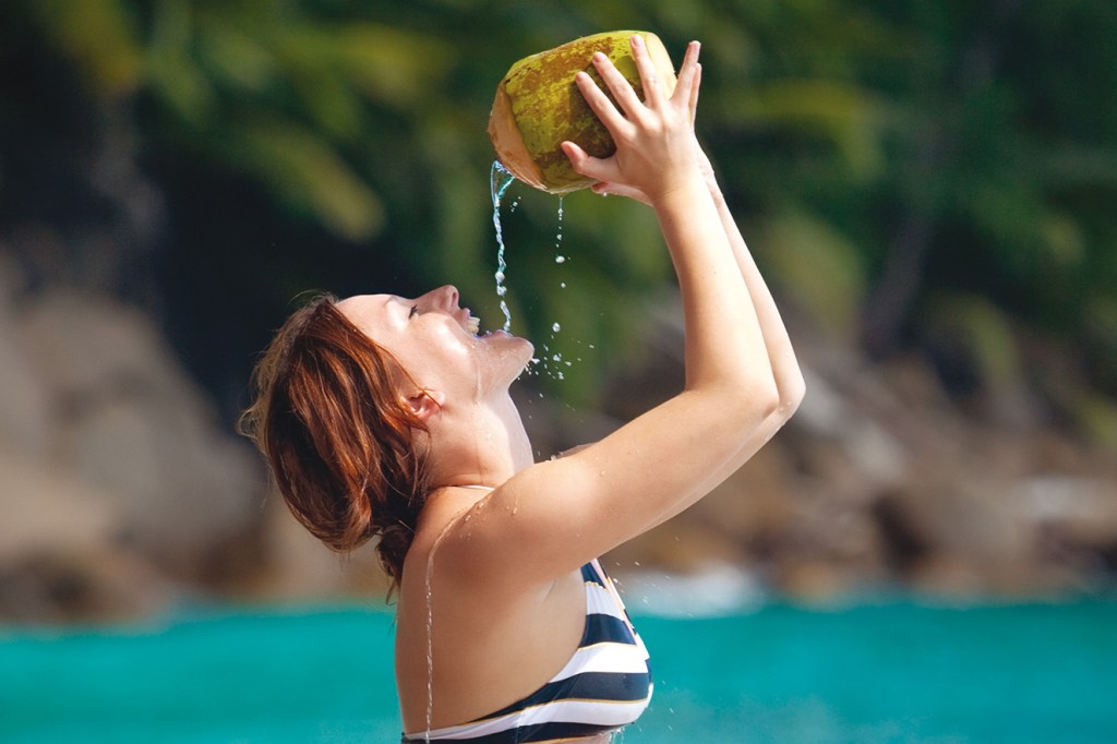 Mulher se refresca na praia com água de coco.
