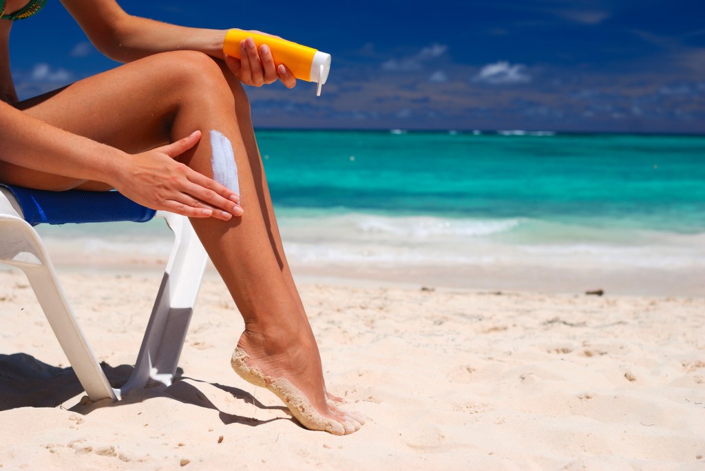 Mulher na praia passando protetor solar na perna