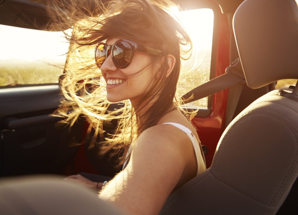 Mulher com cabelos ao vento e sorrindo dentro de carro