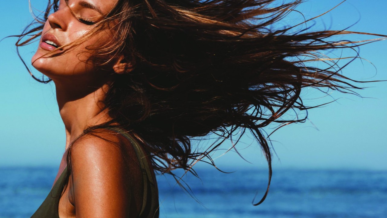 Mulher na praia com cabelos ao vento