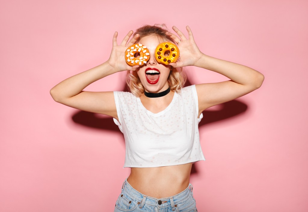 Mulher em fundo colorido segurando dois donuts no rosto