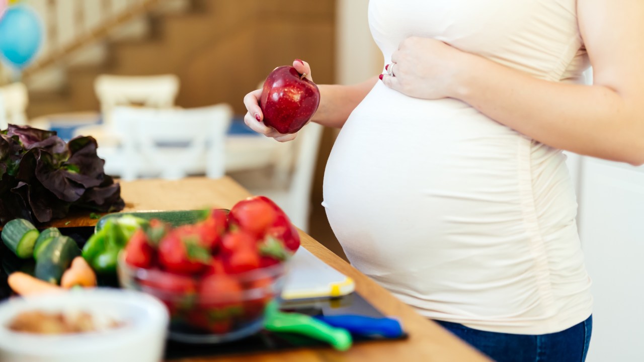 Mulher grávida comendo frutas, como maçã