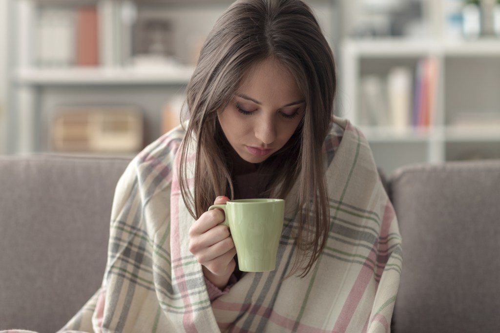 Mulher segunrando xícara de chá e no cobertor