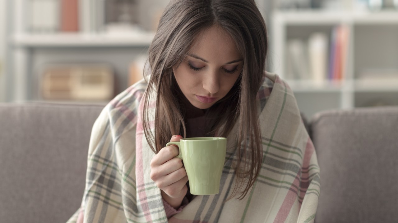 Mulher segunrando xícara de chá e no cobertor