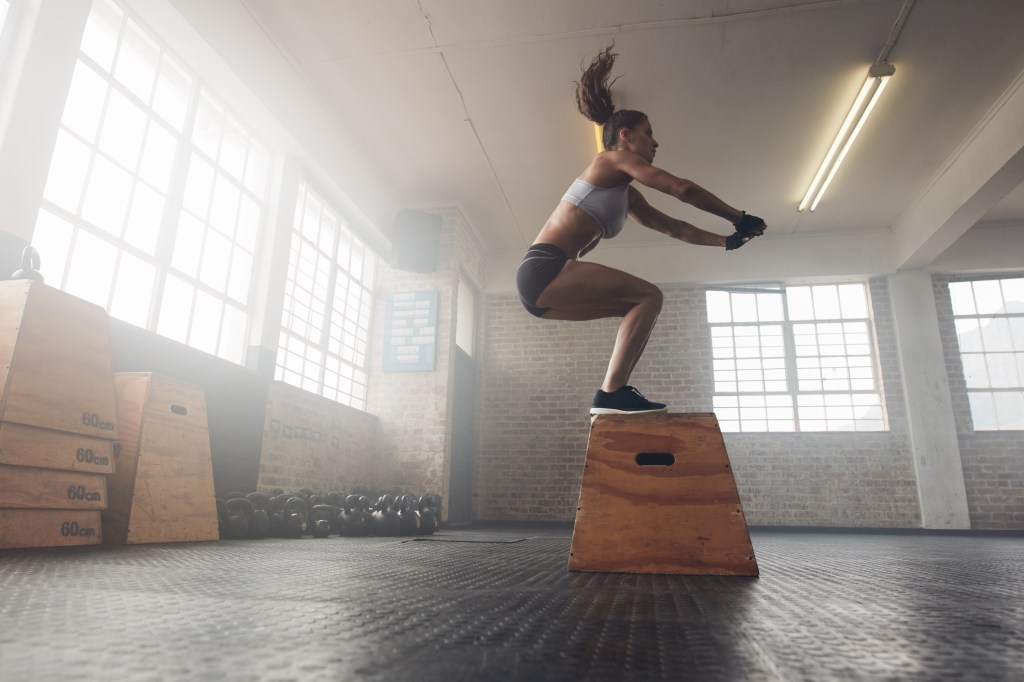 Mulher na academia pulando sobre uma caixa de madeira
