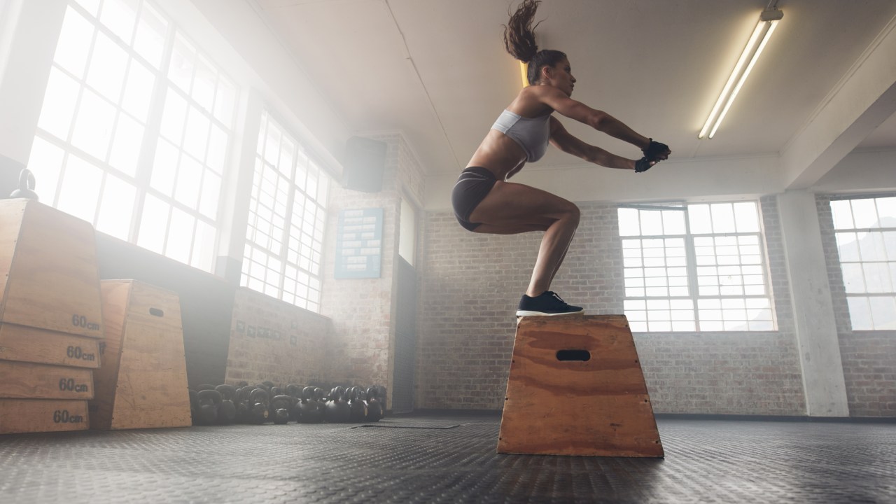 Mulher na academia pulando sobre uma caixa de madeira
