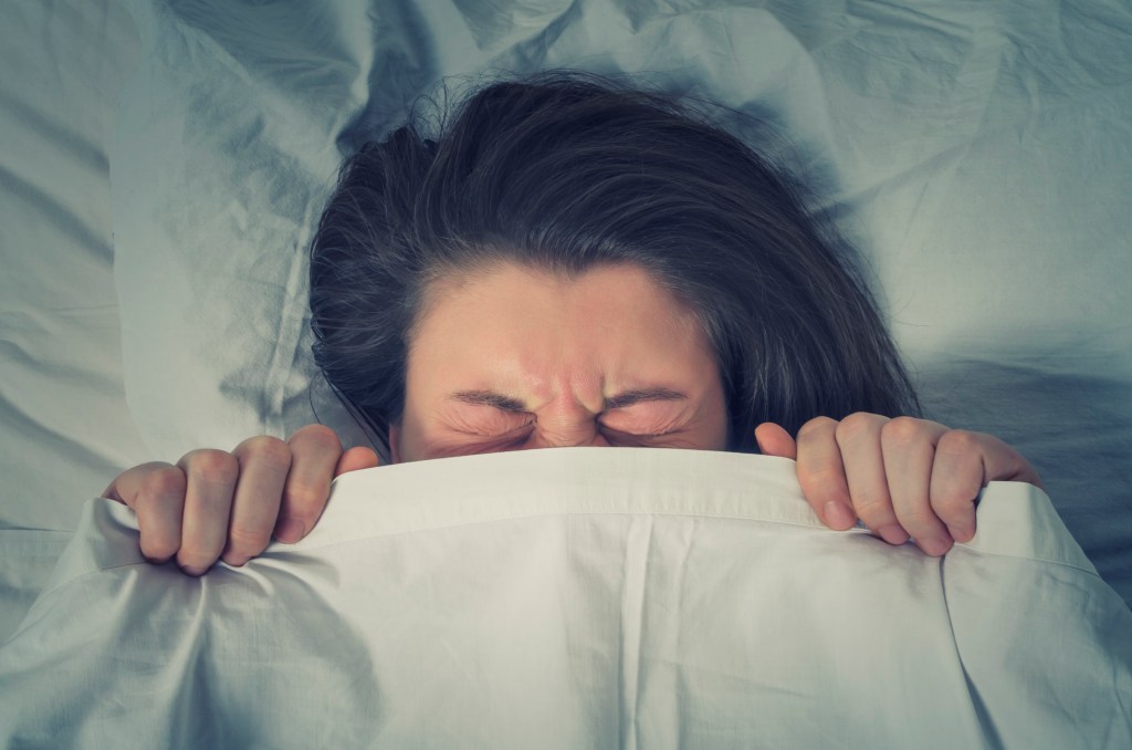Mulher escondida sob o lençol deitada na cama