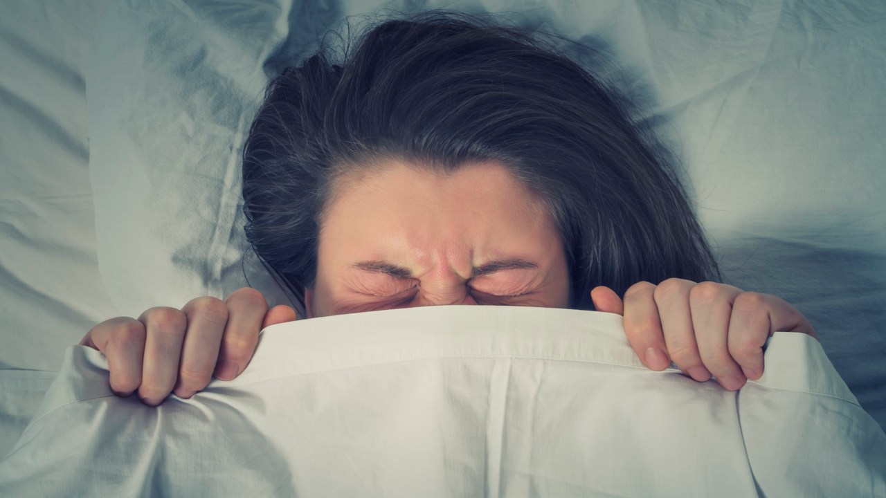 Mulher escondida sob o lençol deitada na cama