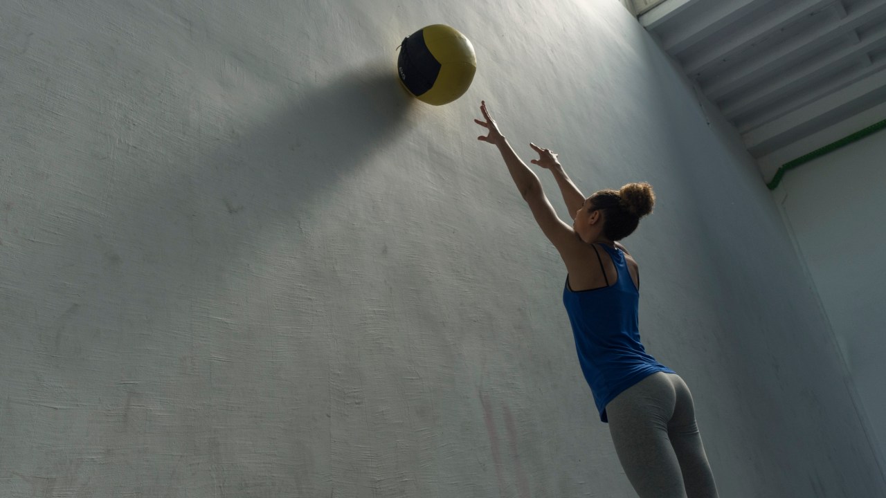 Mulher jogando uma bola na parede no exercício de wall ball