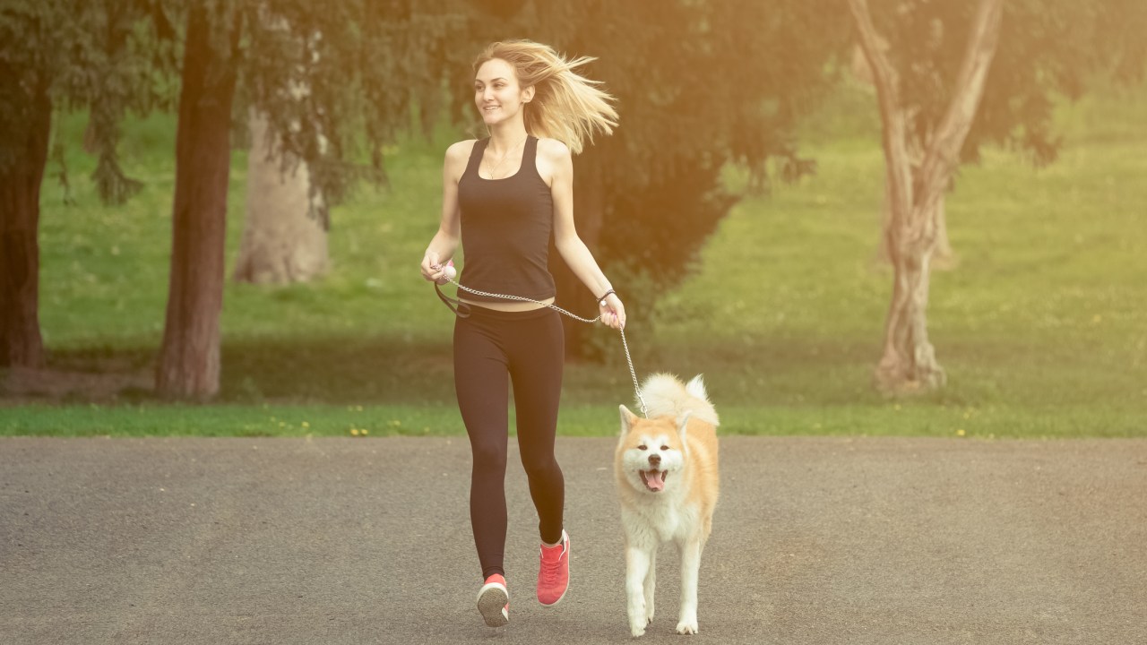 Mulher com roupa de ginástica correndo com cachorro