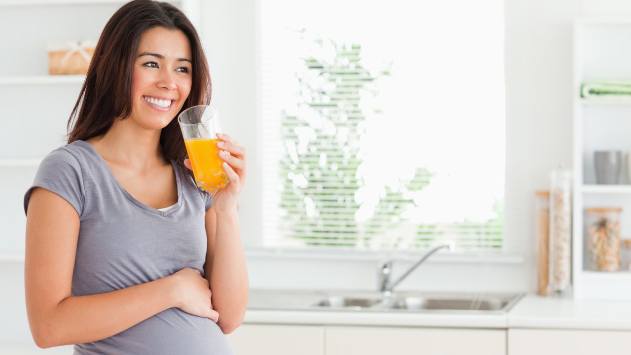 Mulher grávida bebendo um suco de laranja na cozinha | dieta na gravidez