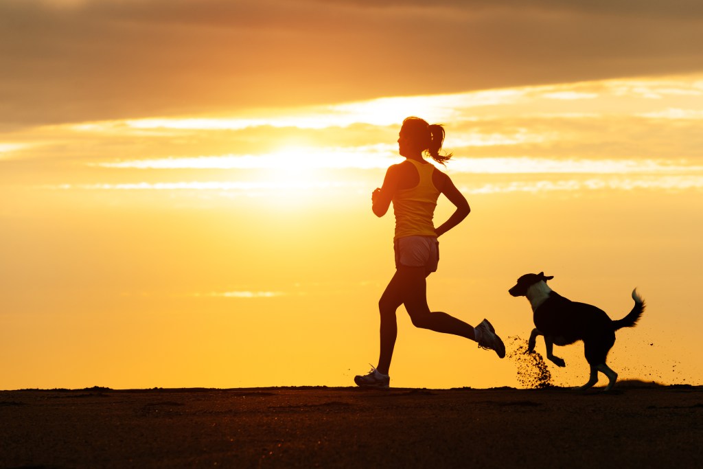 Mulher correndo no pôr-do-sol com cachorro - mindfulness durante a corrida