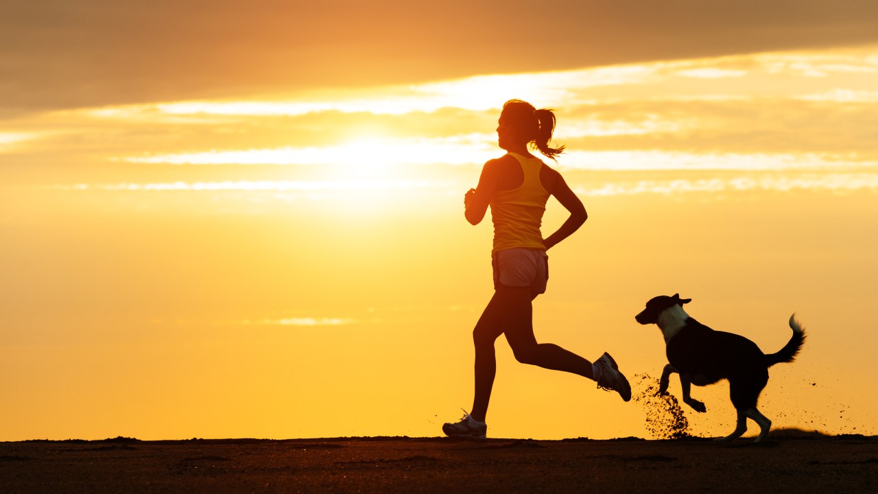 Mulher correndo no pôr-do-sol com cachorro - mindfulness durante a corrida