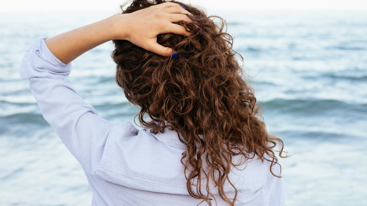 Mulher com cabelo encaracolado de costas olhando para o mar