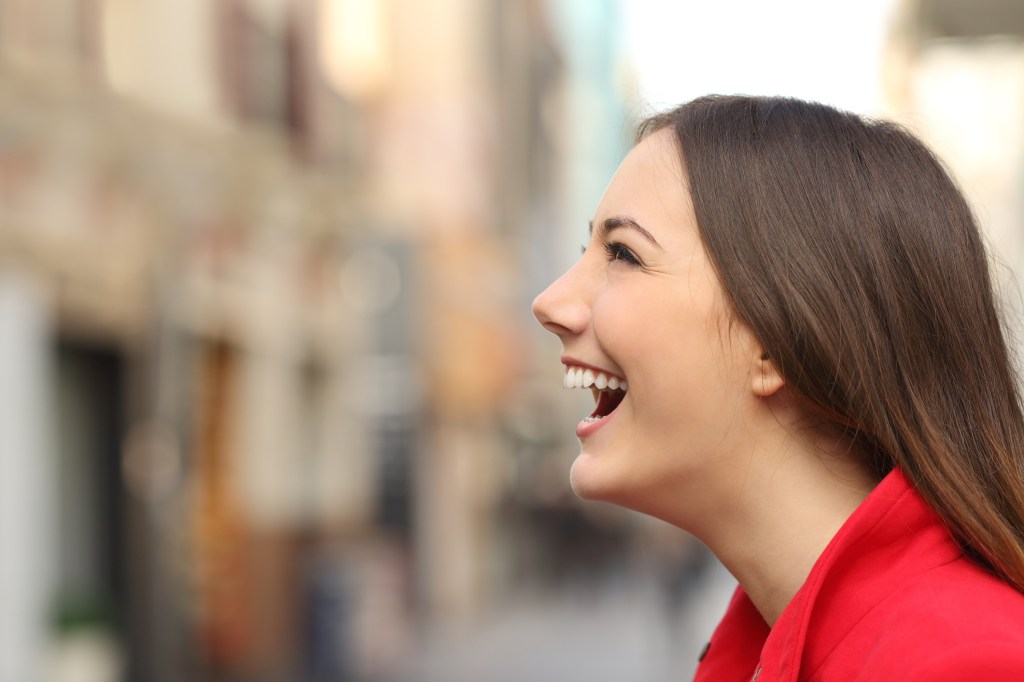 Mulher de perfil sorrindo com roupa vermelha no meio da cidade