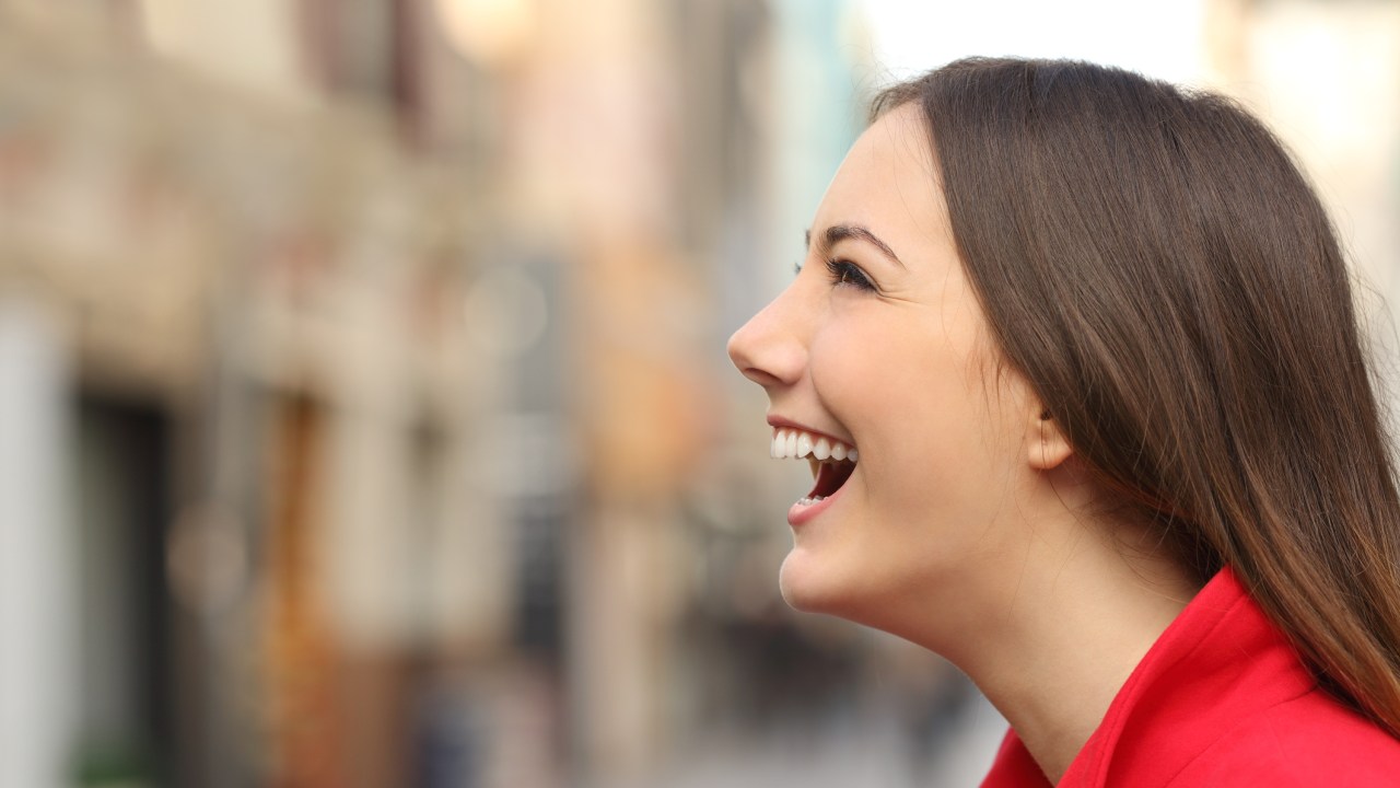 Mulher de perfil sorrindo com roupa vermelha no meio da cidade
