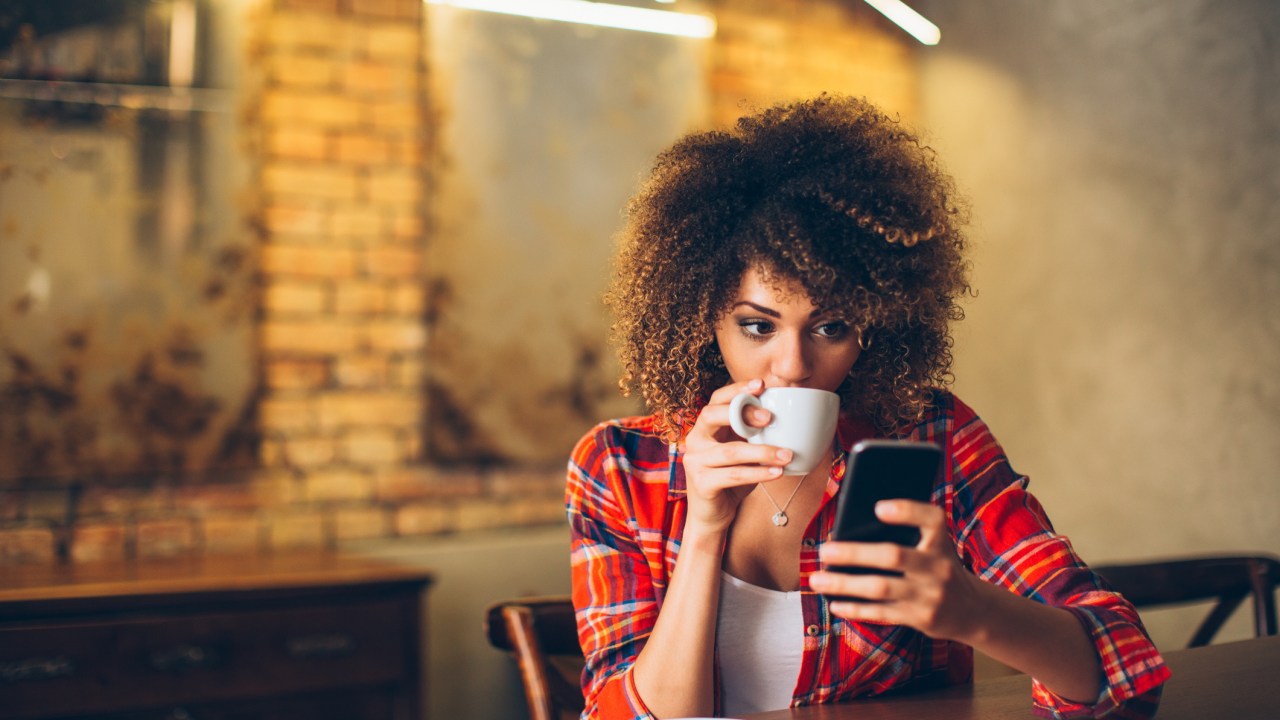 Mulher negra tomando café e olhando o celular