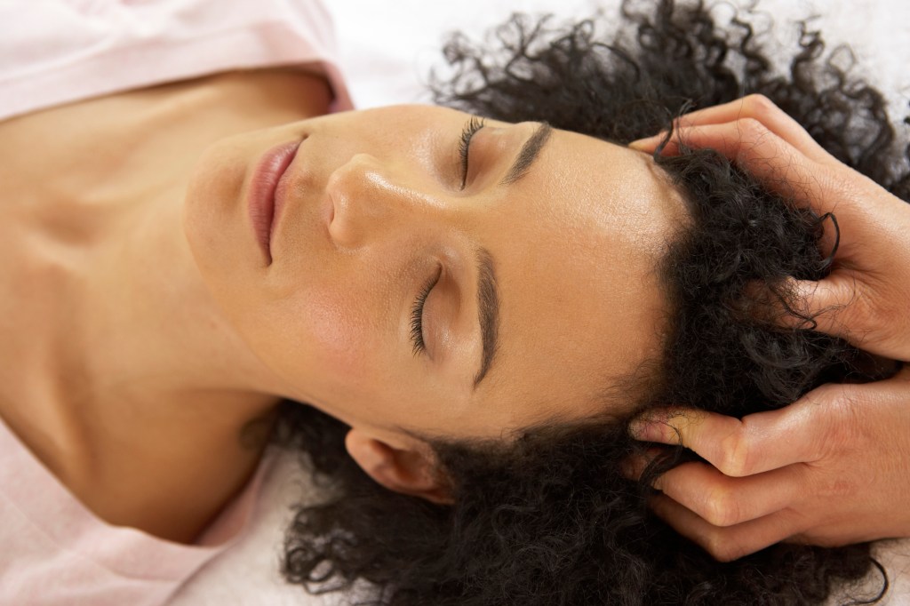 Mulher deitada na maca recebendo massagem no couro cabeludo