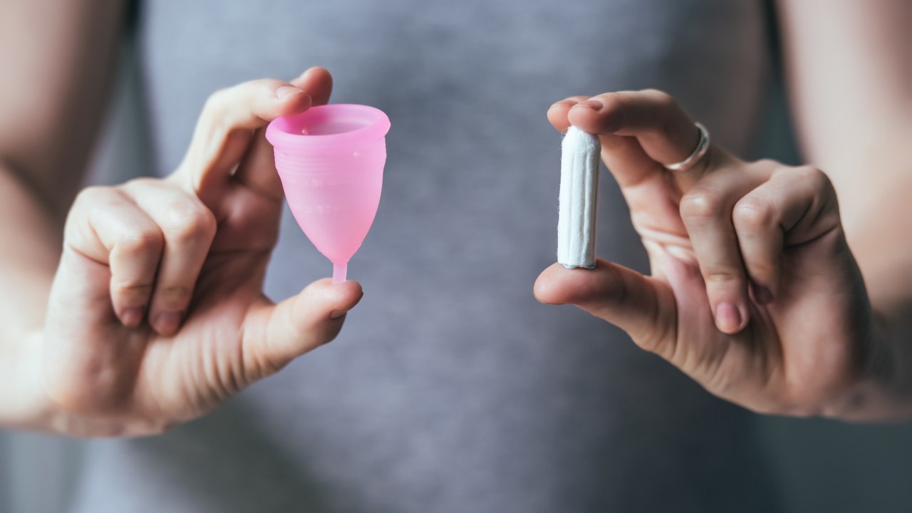 Mulher segurando um copo coletor menstrual em uma mão e um absorvente interno na outra