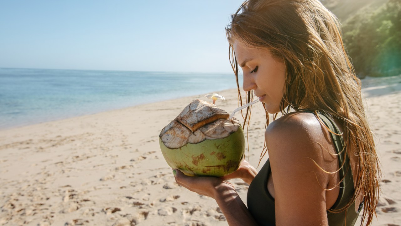 Mulher na praia segurando um coco na mão com o cabelo solto