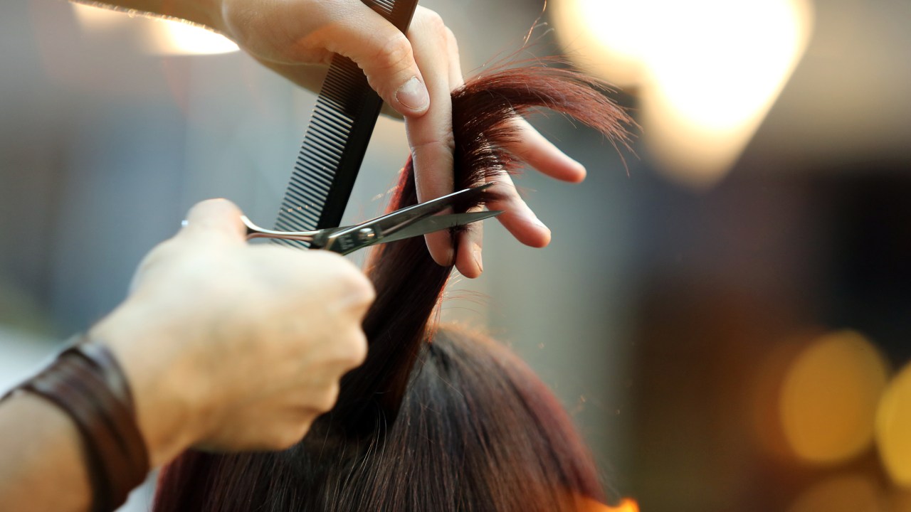 Cabeleireiro segurando um pente e cortando o cabelo de uma cliente