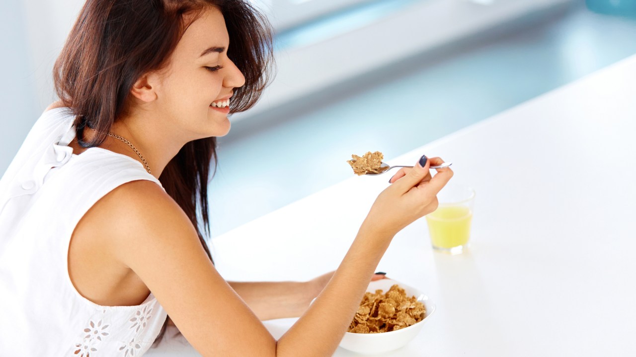 Mulher segurando uma colher com cereal e suco de em uma mesa branca