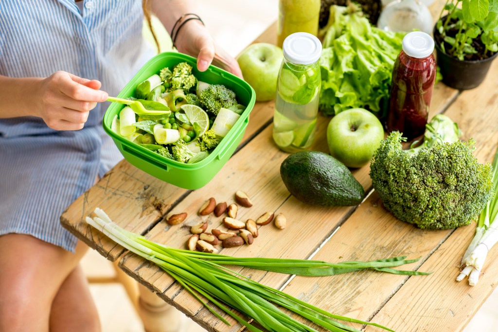 Mulher preparando refeição com legumes e frutas verdes | desintoxicar o organismo