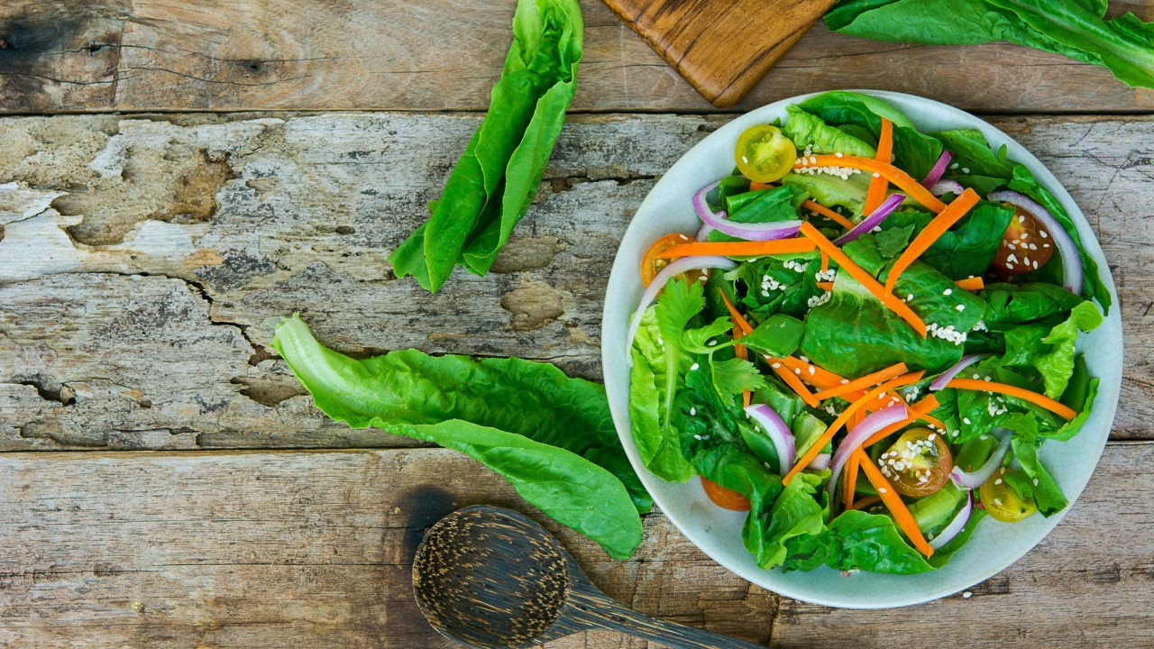 Salada vegetariana com verdes, cenoura e outros vegetais em um bowl sobre uma mesa rústica