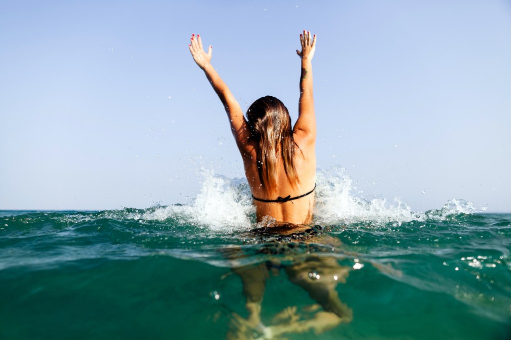 Mulher de biquíni no mar com o cabelo molhado e os braços para cima