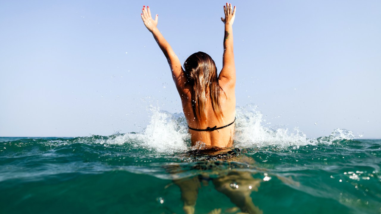 Mulher de biquíni no mar com o cabelo molhado e os braços para cima