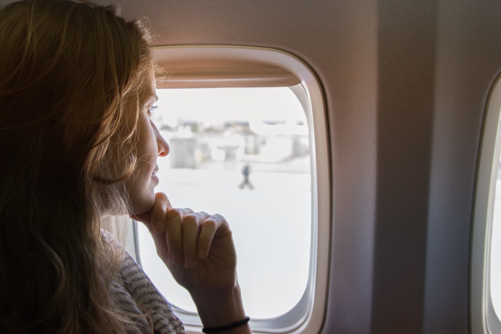 Mulher sentada dentro do avião olhando para fora da janela