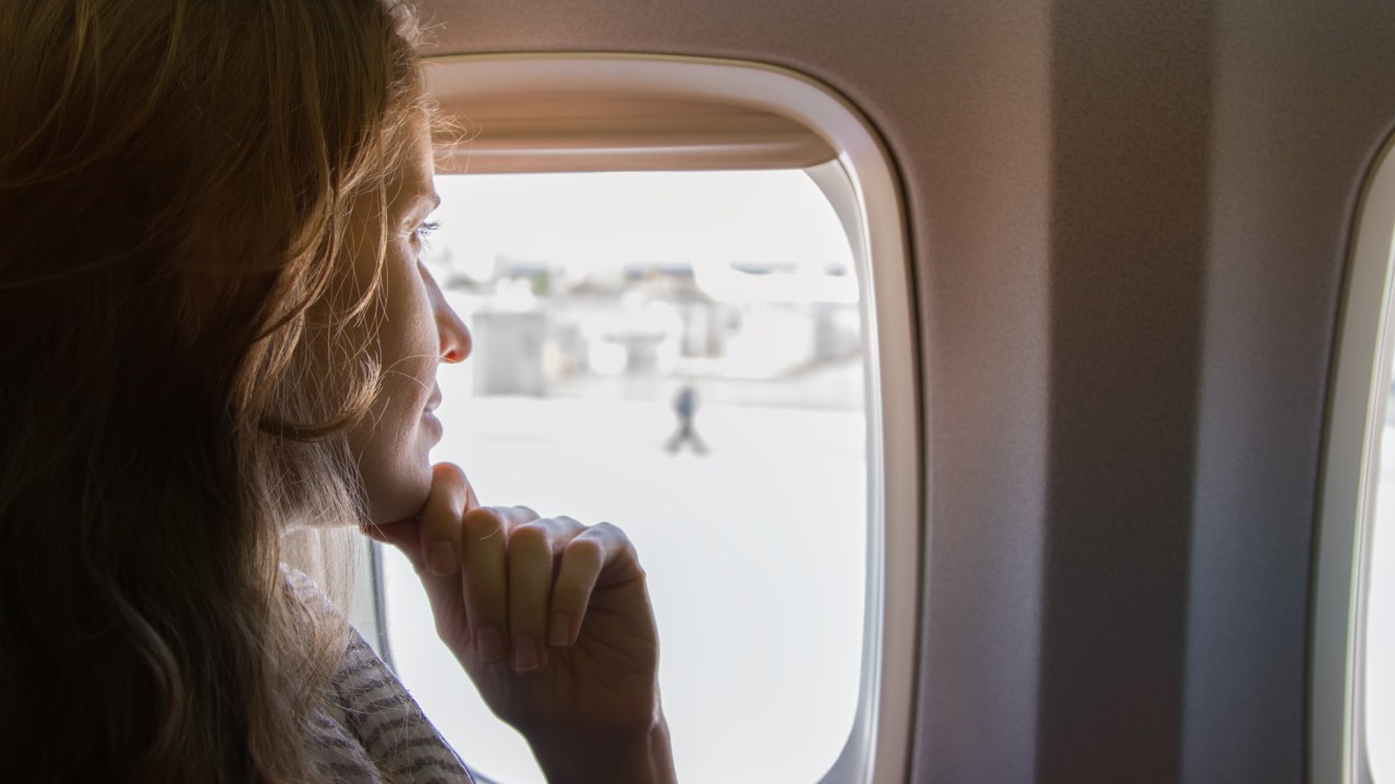 Mulher sentada dentro do avião olhando para fora da janela