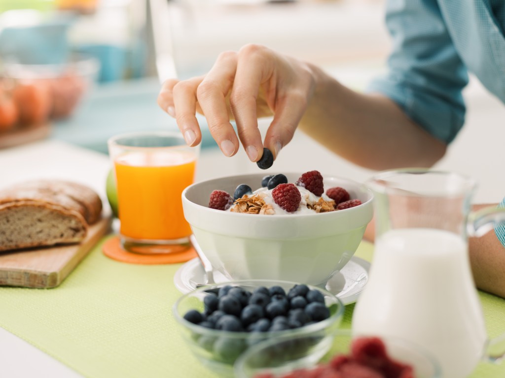 Mulher tomando café da manhã saudável em casa com iogurte e blueberries