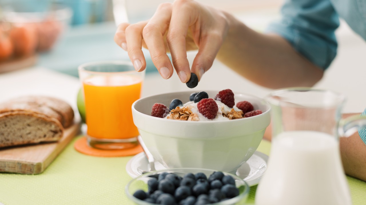 Mulher tomando café da manhã saudável em casa com iogurte e blueberries
