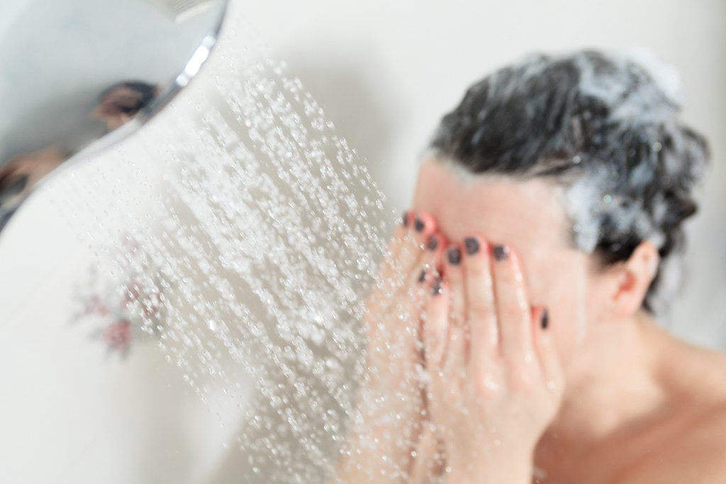 Mulher tomando banho de chuveiro com a mão no rosto