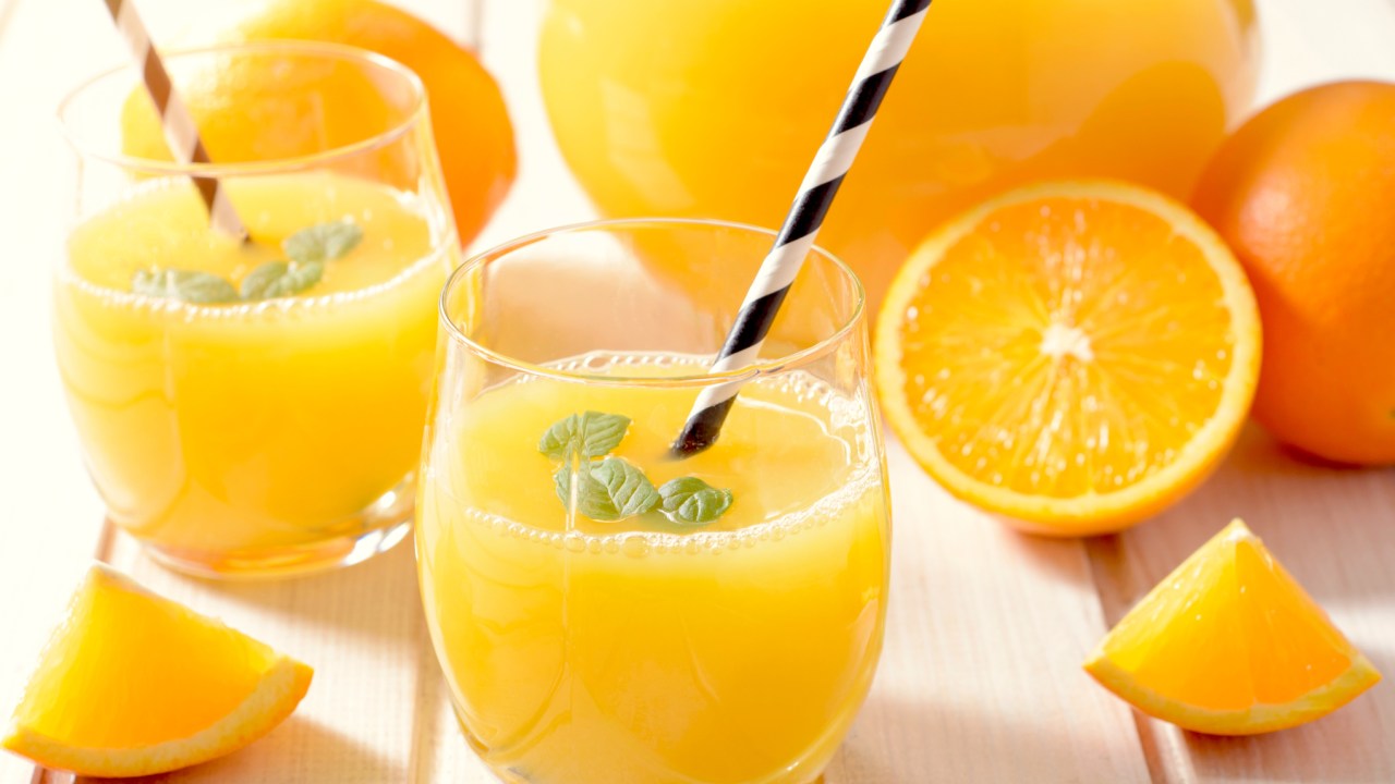 Jarra de suco de laranja com várias frutas cortadas e dois copos com canudo