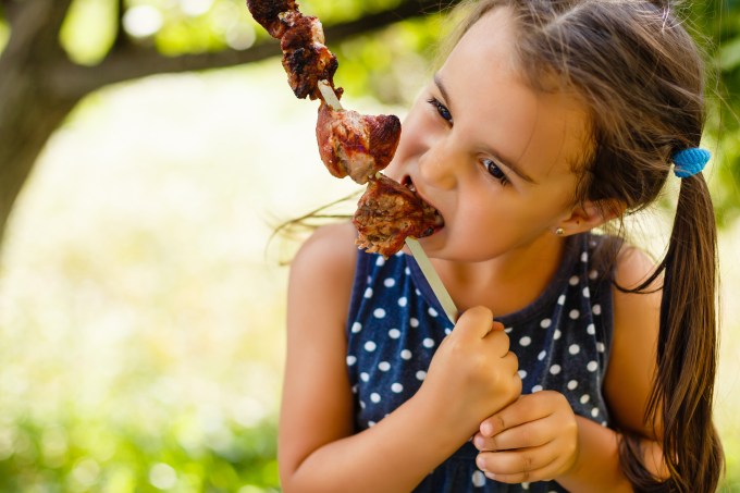 Menina comendo espetinho de carne