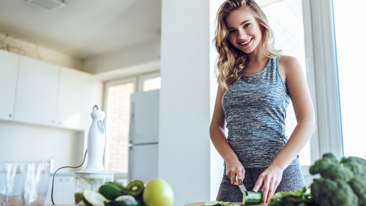Mulher com roupa esportiva preparando uma refeição saudável na cozinha