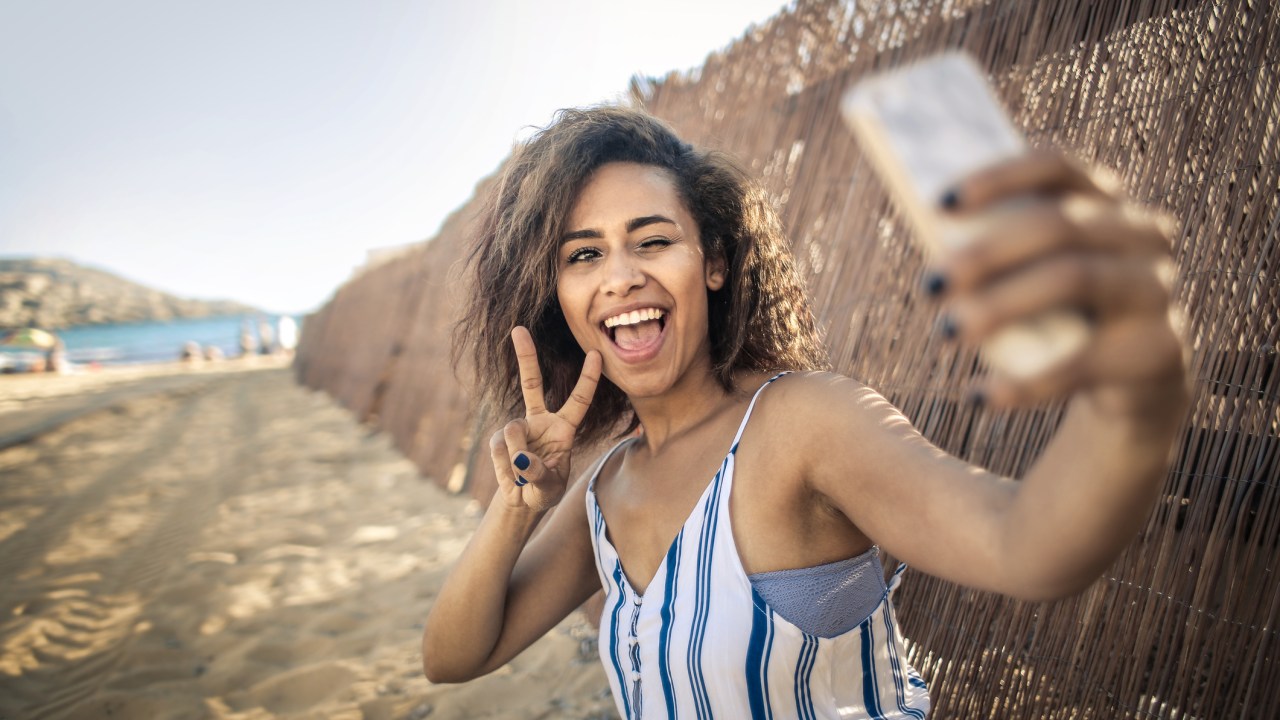 Mulher tirando uma selfie sorrindo na praia