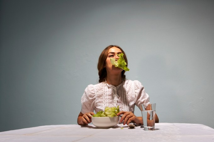 Woman sitting at table, eating lettuce