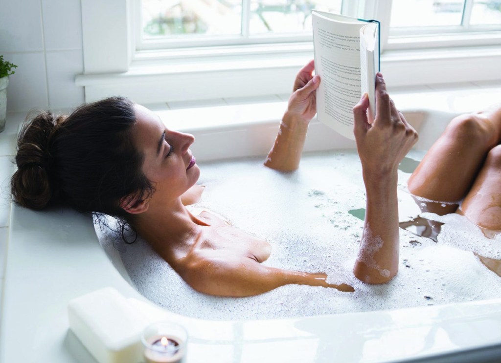 dicas para se desconectar 1 Imagem meramente ilustrativa mostra uma mulher de cabelos escuros tomando um banho de banheiro enquanto lê um livro