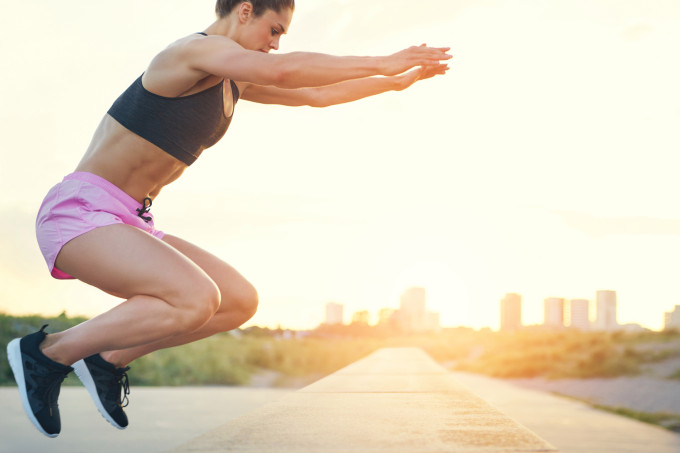 Imagem meramente ilustrativa mostra uma mulher de top e short rosa realizando agachamento com salto - 6 exercícios sem peso para perna e bumbum