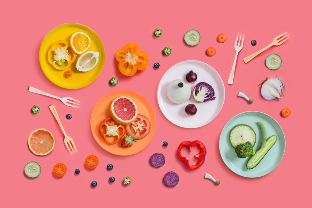 Estilo minimalista de foto com comidas de origem vegetal em um fundo rosa com pratos nas cores amarelo, laranja, branco e verde