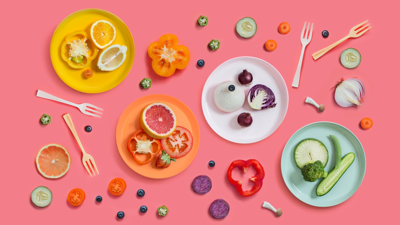 Estilo minimalista de foto com comidas de origem vegetal em um fundo rosa com pratos nas cores amarelo, laranja, branco e verde
