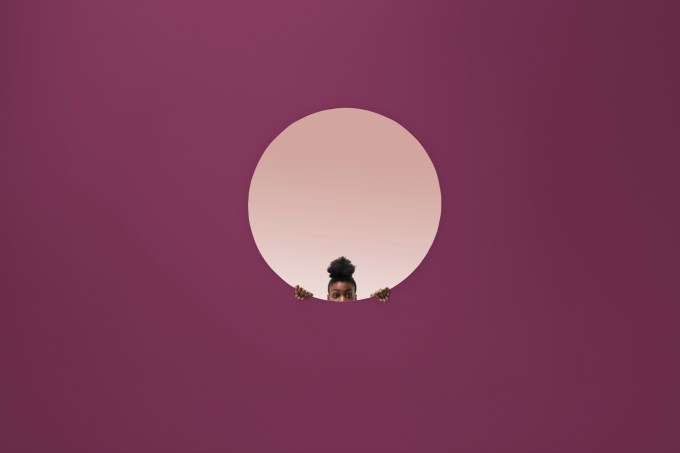 Woman peeking out of round opening in coloured wall