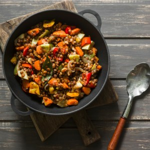 Salada de lentilha com vegetais em um prato escuro, com uma colher de metal com o cabo marrom ao lado