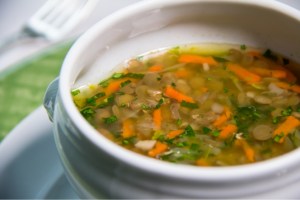 Sopa de lentilha em um recipiente branco, de porcelana com um garfo no fundo da imagem