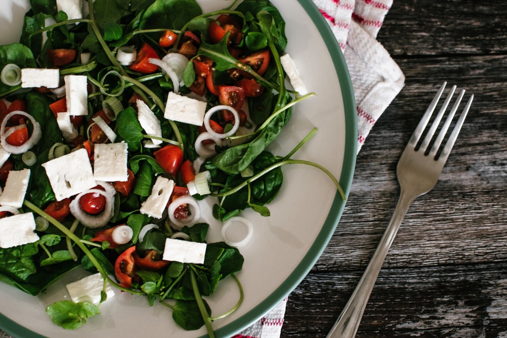 Salada de rúculas com tomate e tofu em um parto branco com borda verde e um garfo ao lado - receitas de salada proteicas