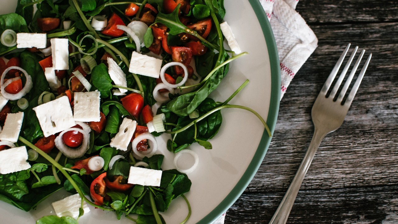 Salada de rúculas com tomate e tofu em um parto branco com borda verde e um garfo ao lado - receitas de salada proteicas